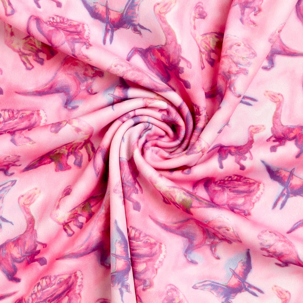 Close-up fabric swatch of pink dinosaur print – soft, stretchy polyester with colorful prehistoric illustrations