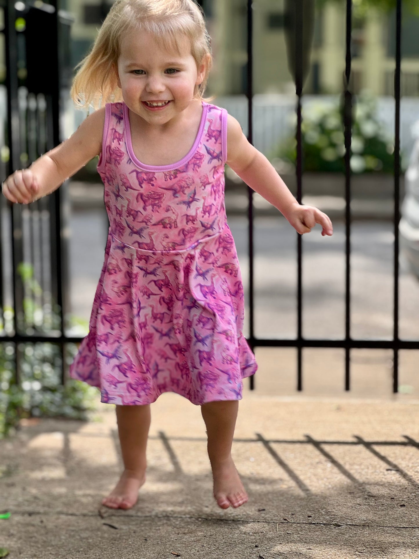 Child in girls summer dino dress with arms raised and big smile – perfect for playdates, parties, and everyday fun