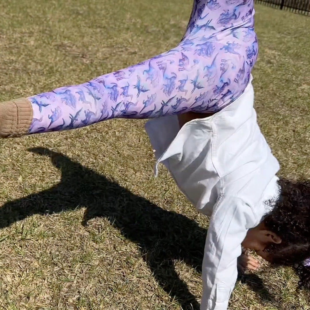 Child in a handstand on grass with colorful objects in the background
