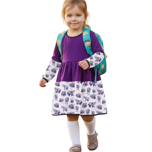 Child wearing a purple dress with animal pattern and green backpack on a white background