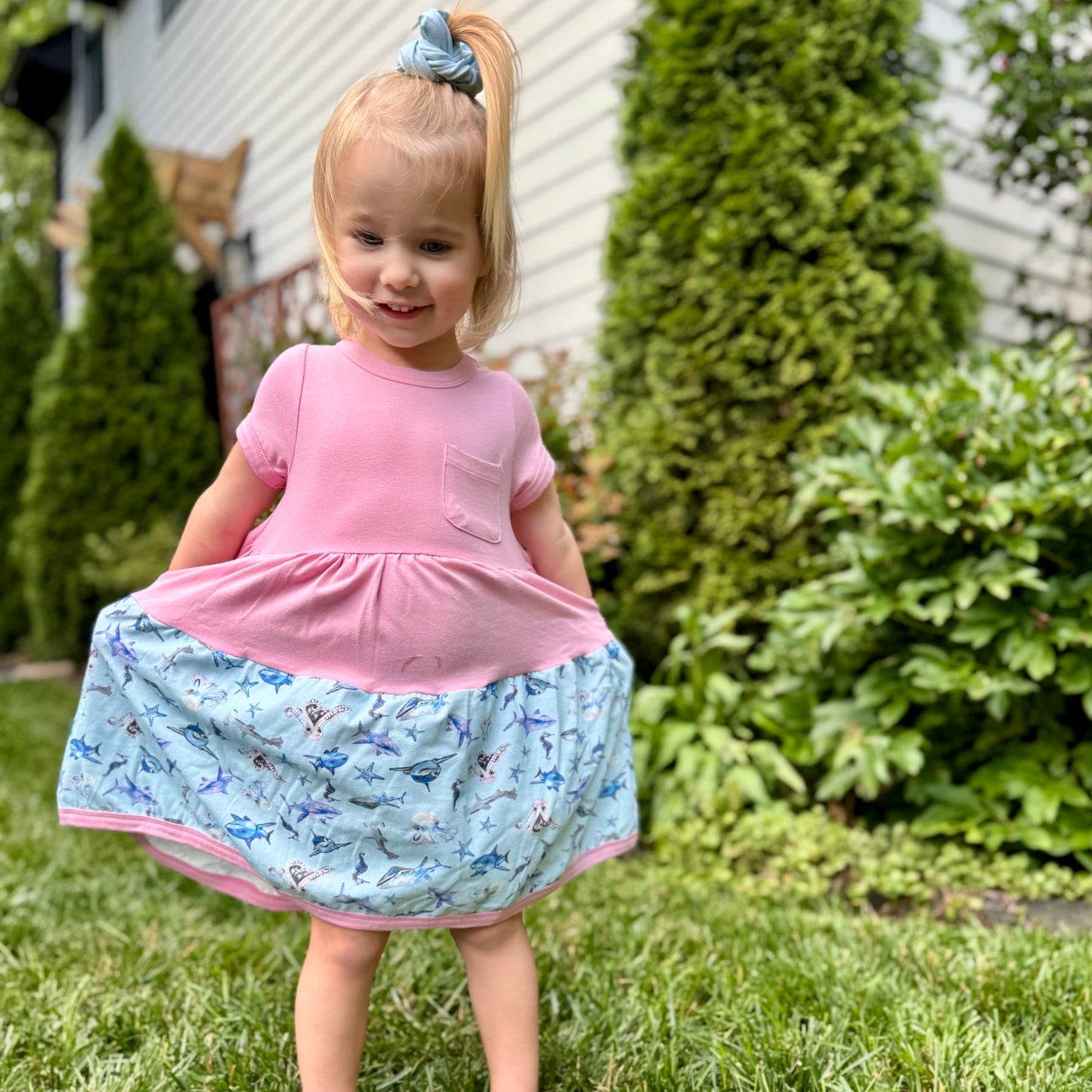Toddler girl wearing pink shark-print dress with matching scrunchie – short-sleeve, sensory-friendly cotton outfit for summer play