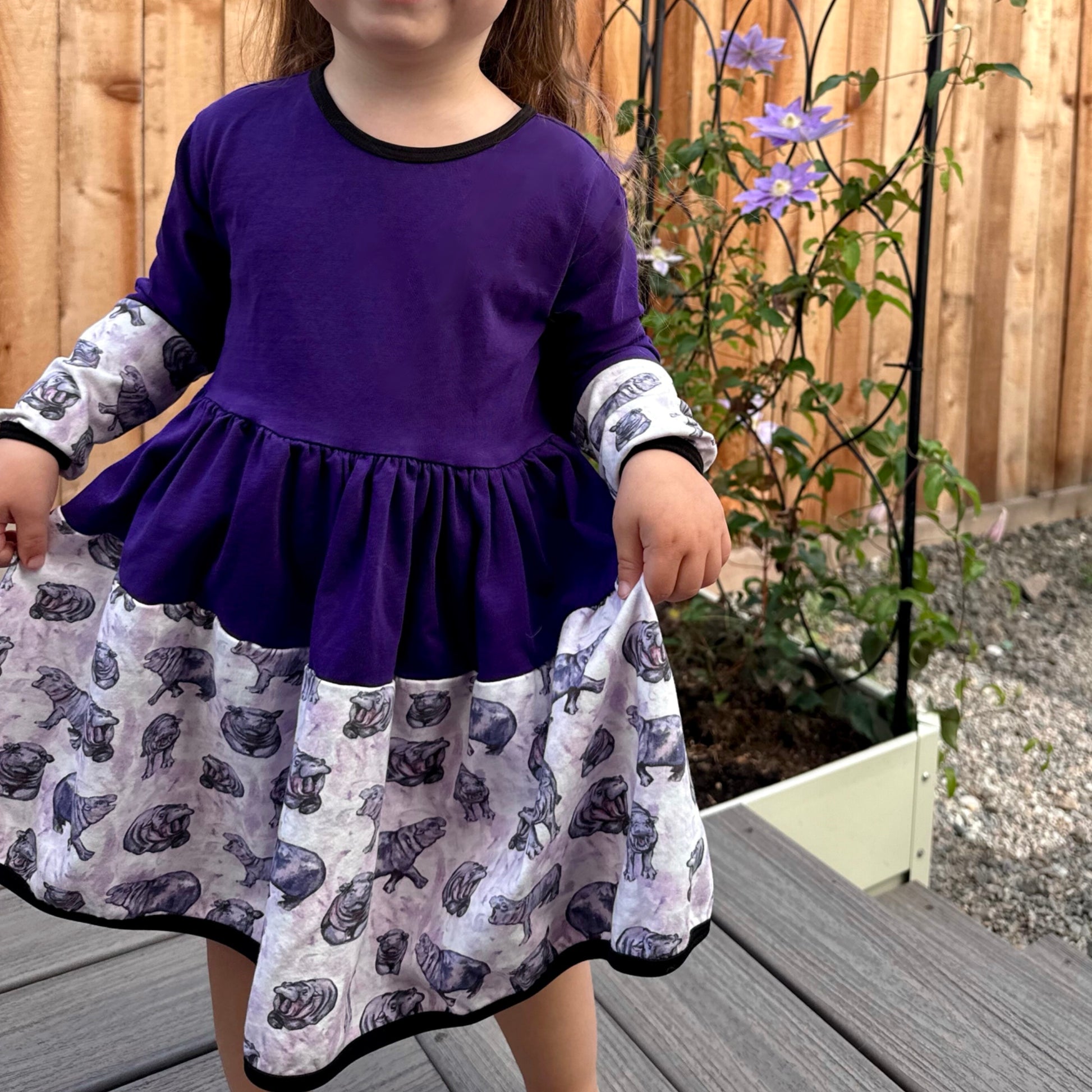 Child wearing a purple dress with a patterned skirt outdoors.