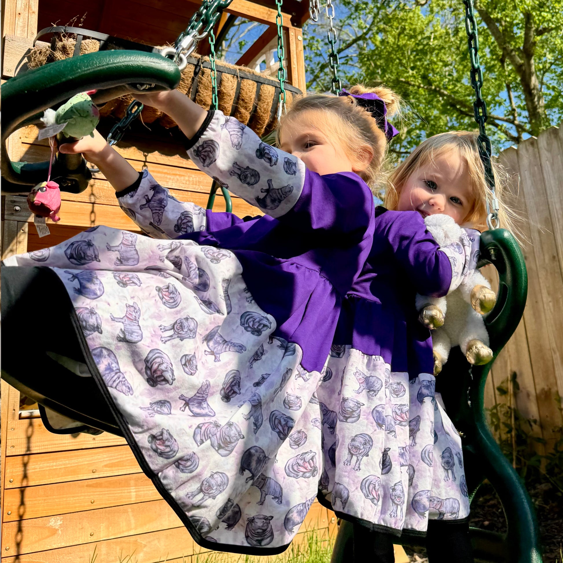 Sisters wearing purple hippo dresses with hand-painted animal designs, enjoying a playful moment outside.
