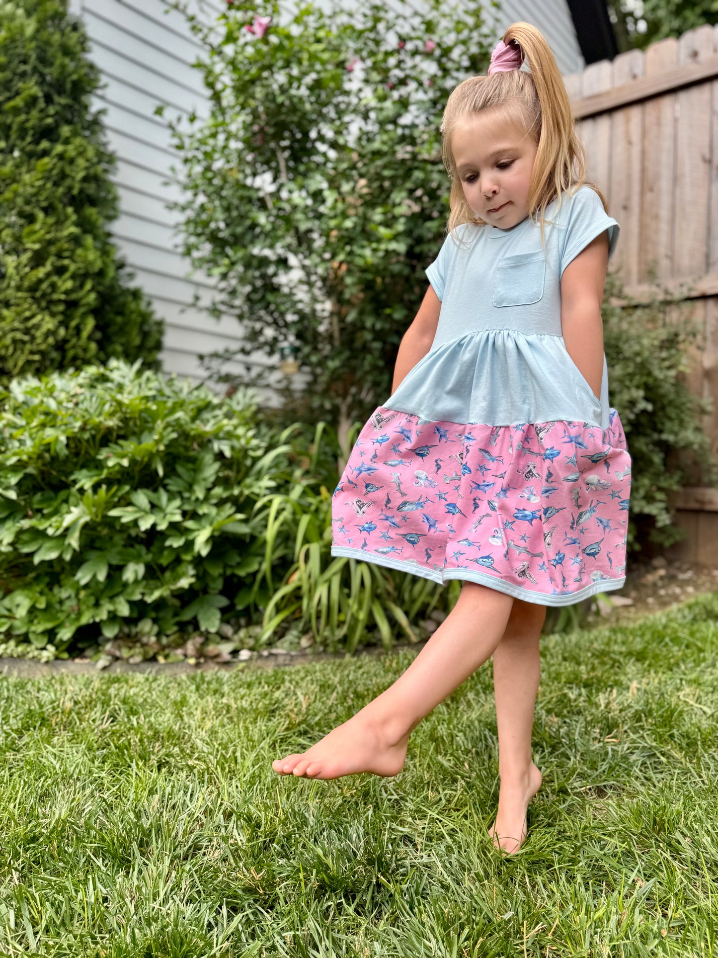 girl wearing blue and pink shark twirl dress standing on grass soft sensory friendly summer outfit for play